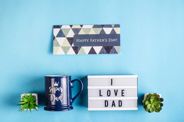 Father's day layout with a gift cup, a card and the inscription I love dad on a decorative lamp on a blue background. Top view, flat lay