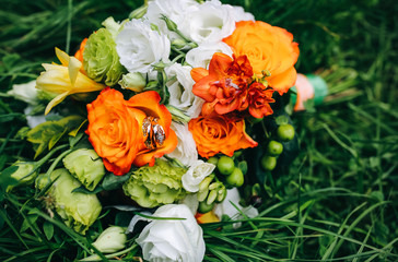 Beautiful wedding bouquet is lying in the grass. Engagement rings are on the flowers. Orange colours of fall and autumn in floral composition.