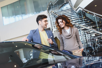 Plakat stylish man in glasses pointing with finger at car near curly attractive woman standing with hand in pocket
