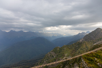 Suspension trail over a precipice and a rainbow in the Caucasus Mountains under a stormy sky, Krasnodar region, Russia