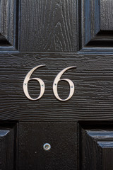 House number 66 with the sixty-six in silver on a plastic black house door with visible grain