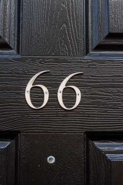 House Number 66 With The Sixty-six In Silver On A Plastic Black House Door With Visible Grain