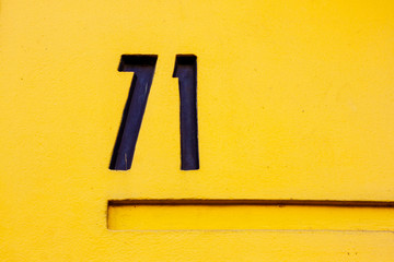 House number seventy-one with the 71 in thick black lines on a bright yellow wall