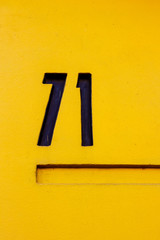 House number seventy-one with the 71 in thick black lines on a bright yellow wall