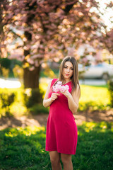 Portrait of charming girl in a fuchsia dress. She hold a flowers of sakura in her hands. Background of japanese tree