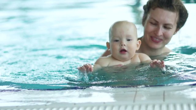 Baby and his mother are swimming in the water by the side of the indoor pool. Development of babies up to one year, immunity strengthening, sports for babies