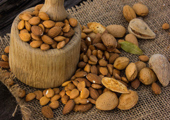 Almonds in a wooden cup on a burlap cloth background. Golden almond closeup in dark brown cup