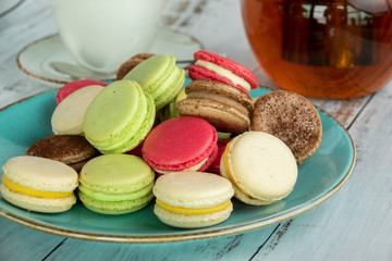 Dessert macaroons on a plate with a kettle of tea