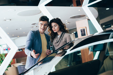 cheerful man pointing with finger at red automobile near attractive woman