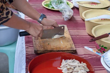 Foto op Canvas woman cut chicken meat fillet. Vegetable on the bench. Butcher cutting pork meat on kitchen .chopped meat food processing in the kitchen with knife with red chopping board. © kanpisut