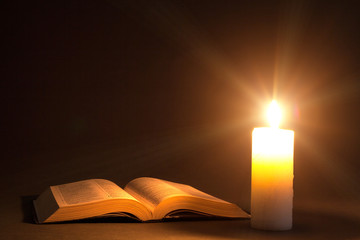 a bible on the table in the light of a candle