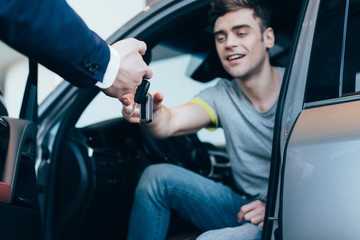 Fototapeta na wymiar cropped view of car dealer giving keys to successful man sitting in car