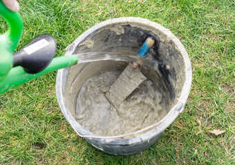 With a watering can, water is poured into a mortar bucket with a trowel to clean bucket and trowel