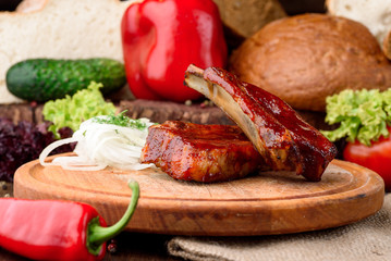 grilled veal ribs on a wooden round board against the background of fresh vegetables. close-up. space