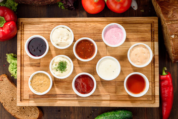 Assorted sauces: ketchup, perigueux, lesser, soy sauce, pesto, berry sauce, Dijon, bechamel in white sauce boats on a wooden background with vegetables. Top view. Close-up. Space