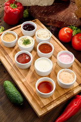 Assorted sauces: ketchup, perigueux, lesser, soy sauce, pesto, berry sauce, Dijon, bechamel in white sauce boats on a wooden background with vegetables. Top view. Close-up. Space