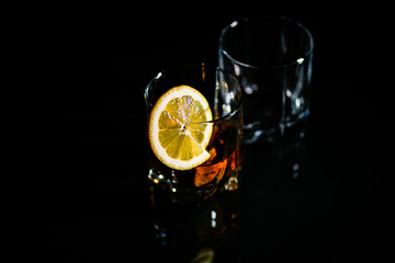 glasses of whiskey on a glass table with a lemon isolated on a black background, special stones for whiskey. glass objects