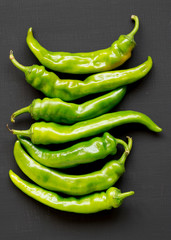 Green chili peppers on black surface, top view. Flat lay, from above, overhead. Close-up.