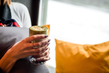 Young girl sitting near the window with cup of coffee or matcha latte. Concept Morning coffee. Close up. Space