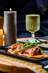 Roasted meat on pumpkin puree with sprouts on a black plate on a table in a restaurant. Matcha latte and candles on background. Close up. Space.