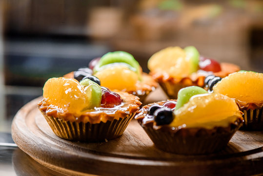 Delicious berry tartlets or cake with with orange, kiwi, and berries on a wooden board closeup. Tasty pastry desserts. close up - Powered by Adobe