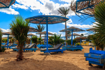 Fototapeta na wymiar Sun umbrellas and chaise lounges on tropical beach. Concept of rest, relaxation, holidays, resort