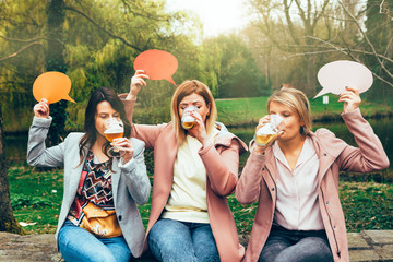 group of girls in the park drinking beer together while holding a thought bubble on their hands....