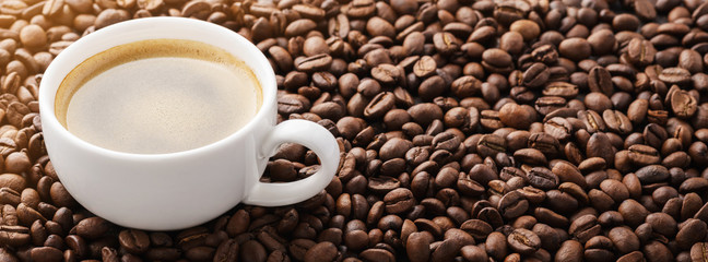 Coffee cup on roasted coffee beans. Warm sunlight.