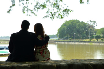 Back view of beautiful couple sitting together in love near lake nice view