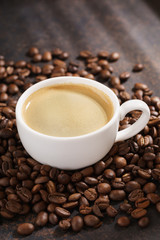 Coffee cup on roasted coffee beans. Dark background, sun rays.