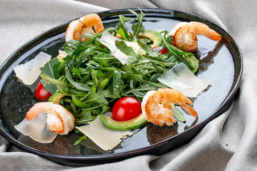 Salad with shrimp, cherry tomatoes, avocado and arugula on textile background