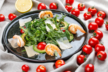 Salad with shrimp, cherry tomatoes, avocado and arugula on textile background
