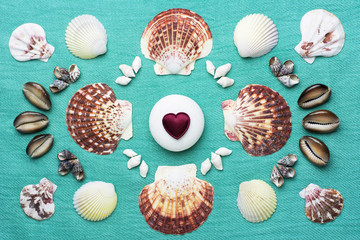 A symetrical pattern made with a collection of shells and white stone with bordo heart in the middle - mint background