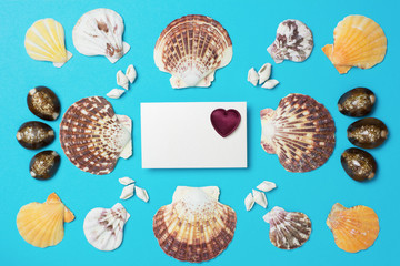 A symetrical pattern made with a collection of shells and white card with bordo heart in the middle - blue background