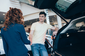 selective focus of happy man and car dealer shaking hands in car showroom