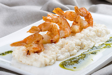 Shrimps with risotto and pesto on a white plate, on a textile background