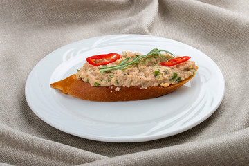Bruschetta with fish tartare on a white plate, on a textile background