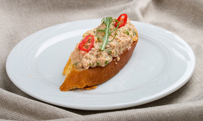 Bruschetta with fish tartare on a white plate, on a textile background