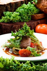 Grilled meat with grilled vegetables and fresh lettuce in teriyaki sauce on a white plate on a dark wooden background, decorated with fresh vegetables and greens. Close-up
