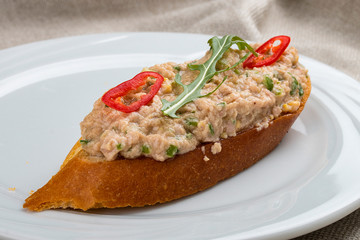 Bruschetta with fish tartare on a white plate, on a textile background
