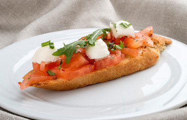 Bruschetta with tomatoes and mozzarella on a white plate, on a textile background