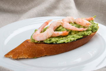 Bruschetta with shrimp and avocado mousse on a white plate, on a textile background