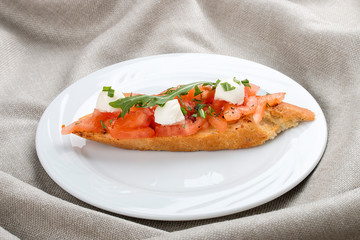 Bruschetta with tomatoes and mozzarella on a white plate, on a textile background