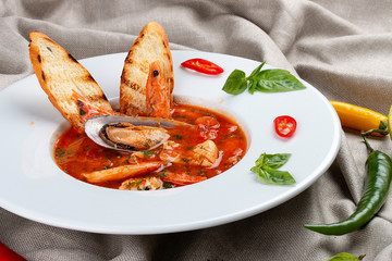 French bouillabaisse fish soup with shrimp, mussels and scallop. In a white plate on a textile...