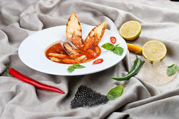 French bouillabaisse fish soup with shrimp, mussels and scallop. In a white plate on a textile background