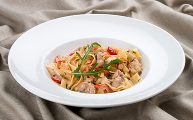 Tagliatelle with rabbit and pepper, with cream sauce in a white plate. On textile background
