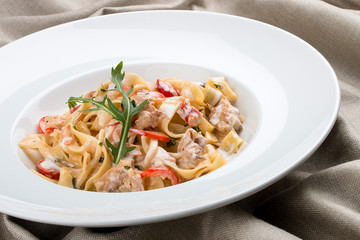 Tagliatelle with rabbit and pepper, with cream sauce in a white plate. On textile background