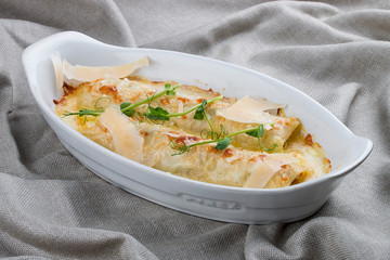 Cannelloni with minced meat, baked in a white ceramic plate. On textile background