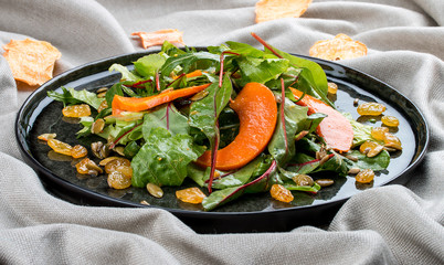 Salad with pumpkin, seeds and raisins on a black plate. Italian cuisine.