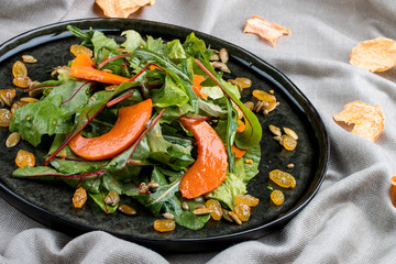 Salad with pumpkin, seeds and raisins on a black plate. Italian cuisine.